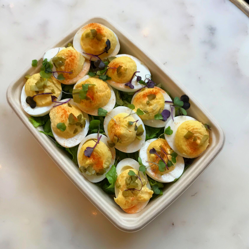 Image is of the deviled eggs catering option on a marble table. Contains 12 deviled eggs on a bed of greens. 