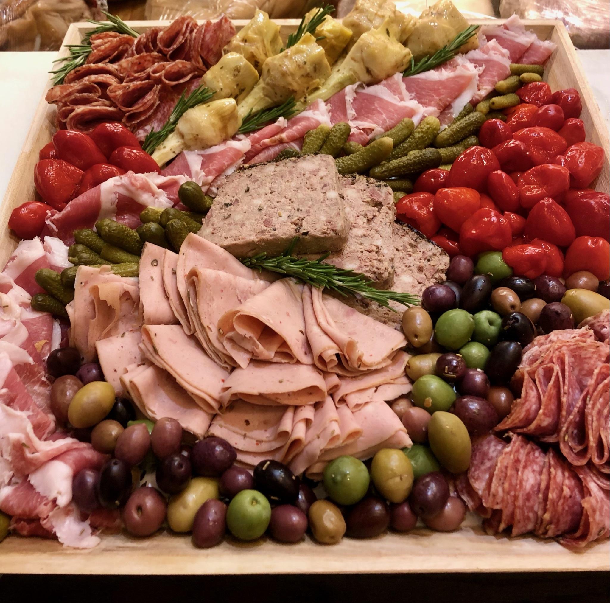 Image of the Charcuterie only meat platter. Assorted cured meats thinly sliced, thick cut pate served with brightly colored olive mixes and pickles.