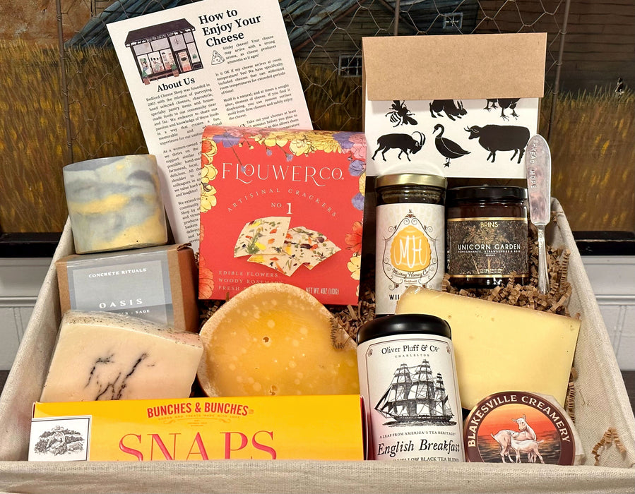 Image is of the Central Park gift basket contents in a wire basket. Includes: candle, honey, jam, crackers, cookies, tea, assorted cheeses, and a card. 