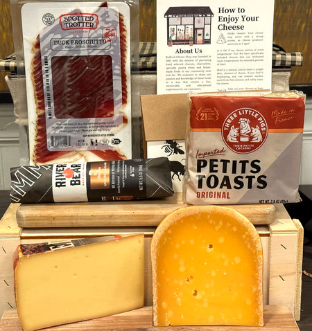 Image is of the Union Square gift basket contents. Including: duck prosciutto, chubs, toast points, cheeses, and a card. 