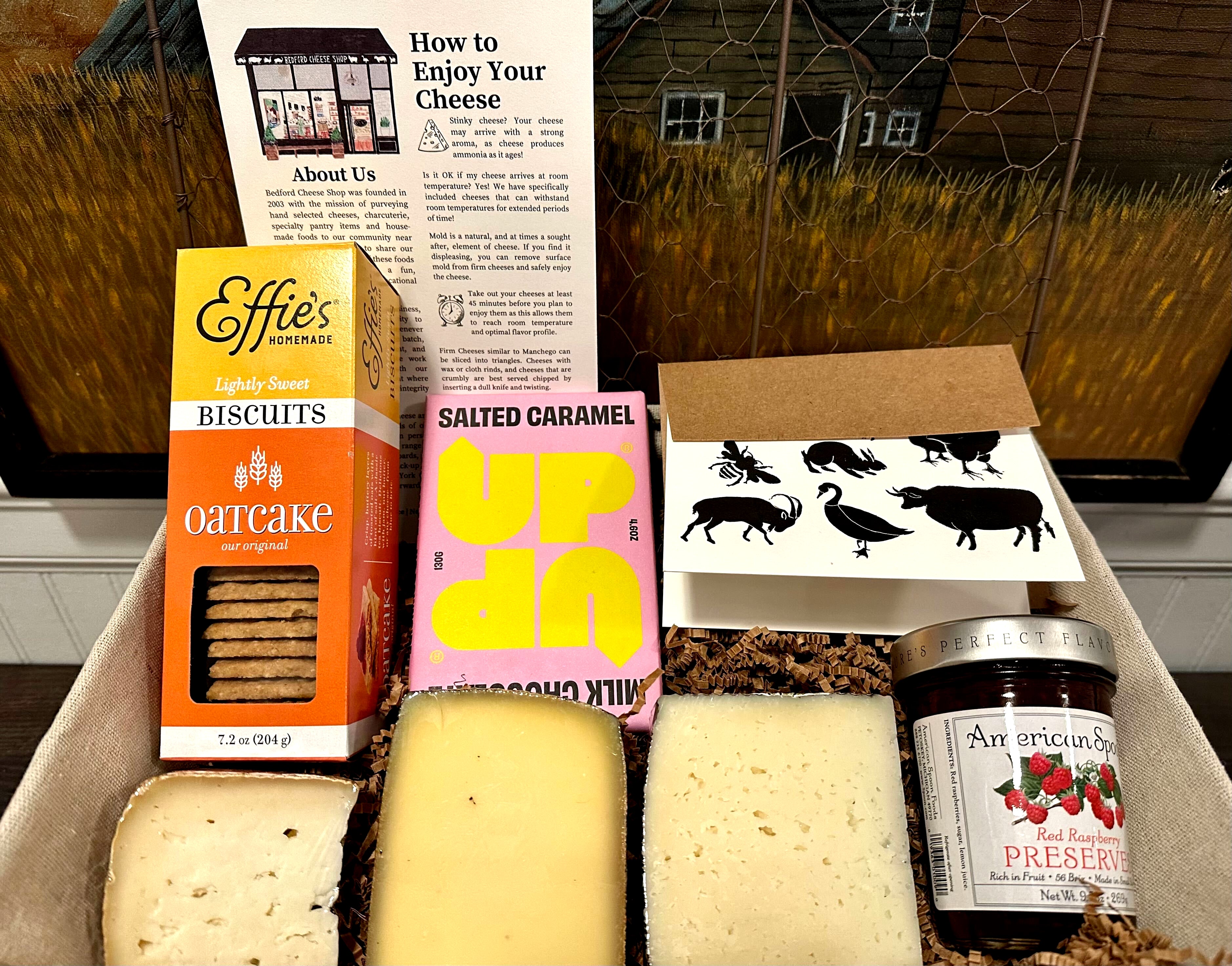 Image of the Madison Park gift basket contents inside the wire gift basket. Includes jam, crackers, chocolate, assorted cheeses, and a card.  