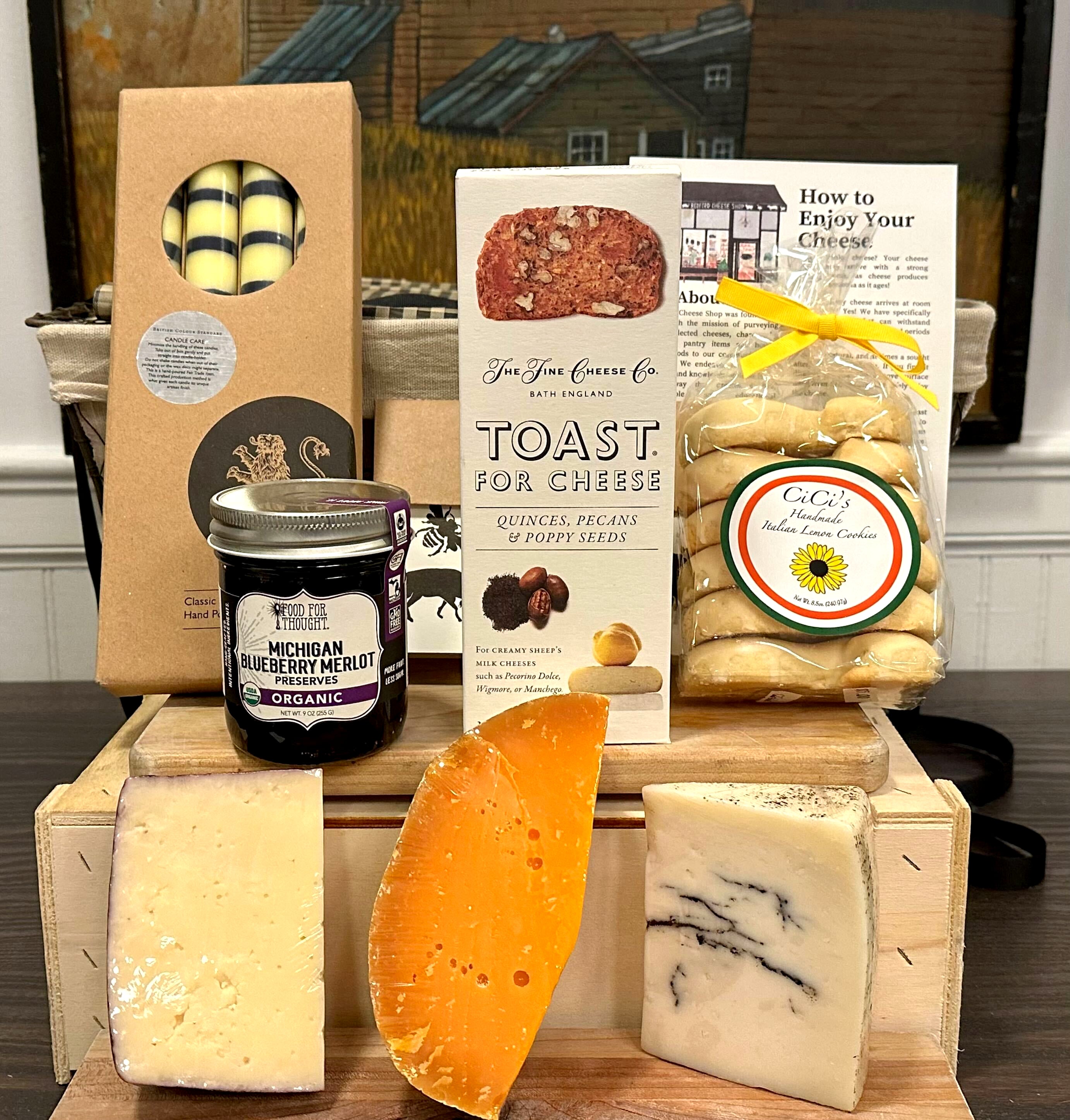 Image of the Bryant Park gift basket contents. Including: cnadle sticks, jam, crackers, cookies, assorted cheeses, and a card.