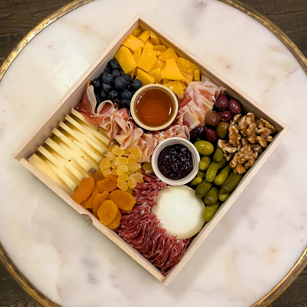 Image is of a three cheese board with two charcuterie upgrades on top of a marble table. 