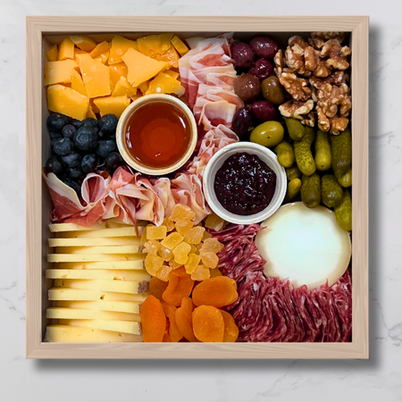 Image is of a three cheese board with two charcuterie upgrades on top of a marble table. 