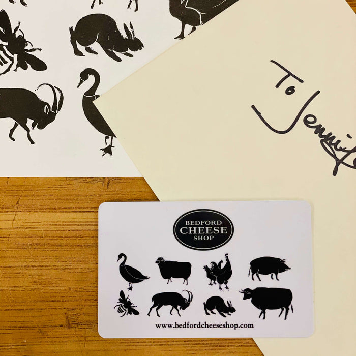 Image is of a Bedford Cheese Shop gift card (white with the BCS black logo and small stylized silhouetted farm animals) on top of a dedicated enveloped and farmhouse card.